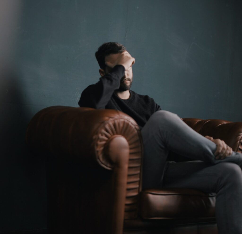 Man sitting on a leather couch with hand on his forehead